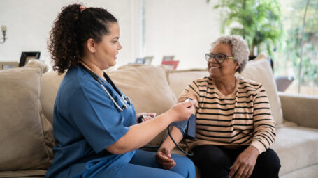 Healthcare worker taking blood pressure of senior woman at home