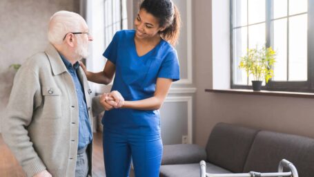 Young caring african nurse helping senior old elderly man grandfather walk . Disable old man trying to walk with the assistance aid of female doctor.