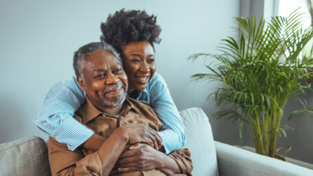 Adult daughter visits senior father in assisted living home. Portrait of a daughter holding her elderly father, sitting on a bed by a window in her father's room.